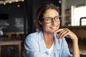 Portrait of beautiful mature woman sitting in cafeteria looking away. Cheerful mature woman wearing eyeglasses thinking with finger on chin. Happy woman relaxing at cafe and smiling.