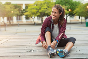 smiling fit woman putting on running shoes