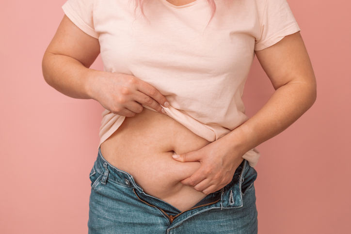 woman with her shirt up grabbing belly fat