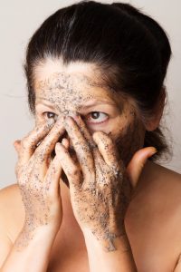 woman applying coffee scrub mask to face