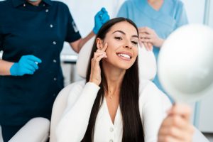 woman looking at her clear skin in a mirror with doctors behind her