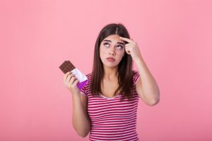 girl holding chocolate with acne on her forehead